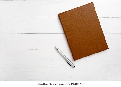 Brown Notebook And Pen On White Table View From Above