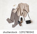 Brown pants in check, beige knitted oversize sweater, cross body bag, black loafers or flat shoes on grey background. Overhead view of women