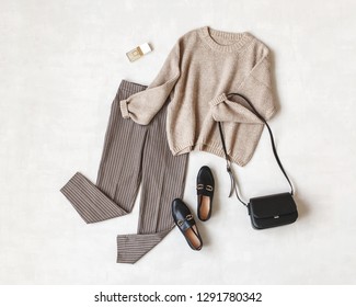 Brown pants in check, beige knitted oversize sweater, cross body bag, black loafers or flat shoes on grey background. Overhead view of women's casual day outfit. Flat lay, top view. Women clothes. - Shutterstock ID 1291780342
