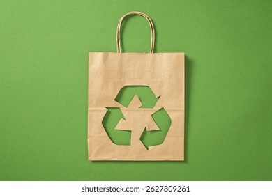 Bolsa de papel marrón con símbolo de reciclaje recortado sobre fondo verde. Compras respetuosas del medio ambiente, concepto de cero residuos.