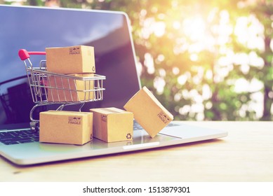 Brown paper boxs in a shopping cart with laptop keyboard on wood table on the public park background.Easy shopping with finger tips for consumers.Online shopping and delivery service concept.