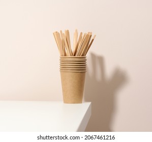 brown paper cardboard cups and wooden stirring sticks on a white table, beige background. Eco-friendly tableware, zero waste