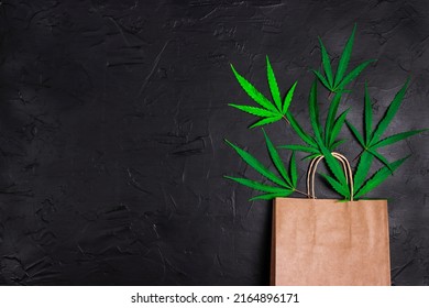 Brown Paper Shopping Bag With Green Marijuana Leaves On Black Background. Copy Space For Text. Medical Cannabis Shopping And Store.