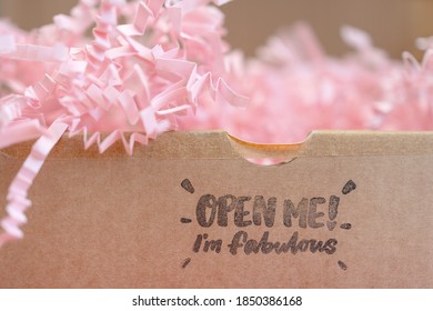 A Brown Parcel Box With Pink Confetti Zig-zag Paper Inside With The Words 'open Me, I'm Fabulous' Printed On The Outside, Shallow Depth Of Field