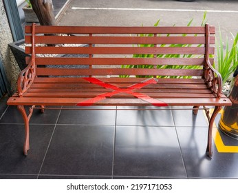 A Brown Park Bench Made Of Wood And Iron With A Red X Sign In The Middle To Indicate Physical Distancing During The Covid-19 Pandemic.