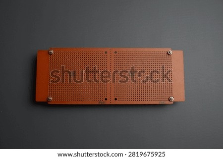 A brown perforated electronic prototype circuit board, or perfboard, is laid flat against a dark gray background.