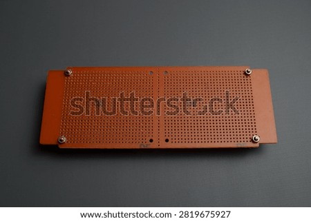 A brown perforated electronic prototype circuit board, or perfboard, is laid flat against a dark gray background.