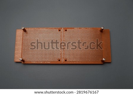 A brown perforated electronic prototype circuit board, or perfboard, is laid flat against a dark gray background.