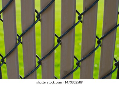 A brown plastic stipe and chain linked fence along the park in the bright summer sun. 