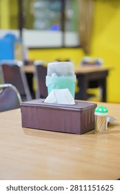 A brown plastic tissue box, toothpick holder, and cutlery container arranged on a restaurant table.