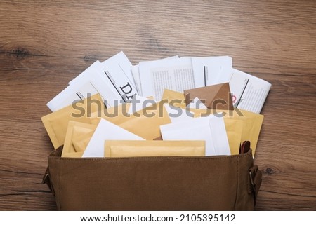 Brown postman bag with newspapers and mails on wooden table, flat lay