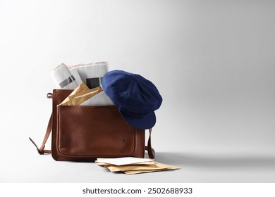 Brown postman's bag, envelopes, newspapers and hat on grey background. Space for text