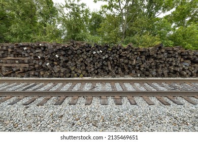 Brown railroad ties piled up next to active train tracks