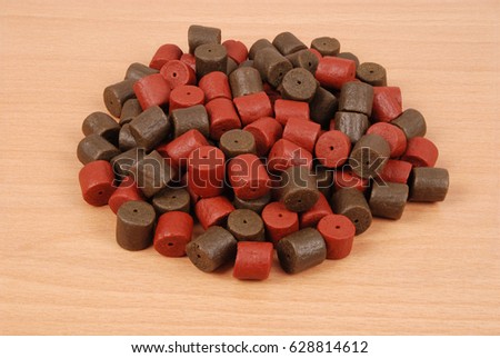 Brown with red pre-drilled halibut pellets for carp fishing isolated on wood background with soft shadow