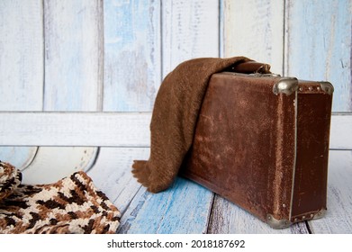 Brown retro suitcase on a blue background, with a dark warm shawl, symbolizing travel, tourism, and a long journey. 