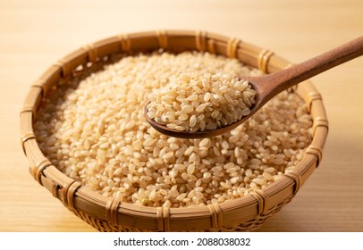 Brown rice in a bamboo colander and a wooden spoon on a wooden background. A pile of brown rice. - Shutterstock ID 2088038032