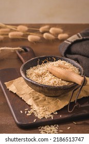 Brown rice in ceramic bowl with wooden scoop on rustic countertop.