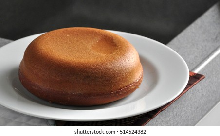 Brown And Round Cake Made From Rice Cooker On White Plate.