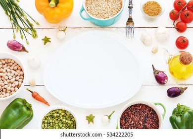 Brown, ruby and black rice in bowls, peas, garbanzo beans, assorted fresh vegetables, olive oil and spices. Empty plate in the middle. Vegetarian meal background. Copy space. - Powered by Shutterstock