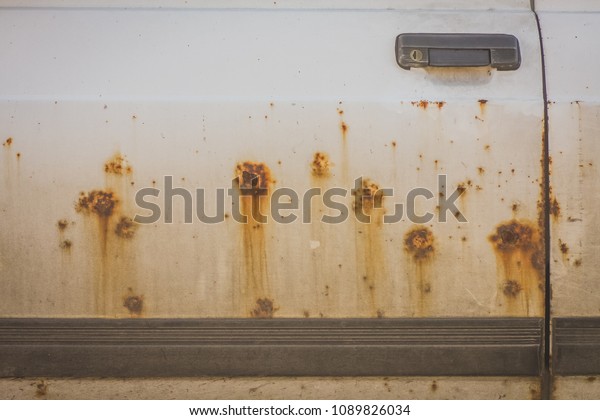 Brown rust patches\
on a white door of a passenger car. Rust eating through a driver\
door of a white car.