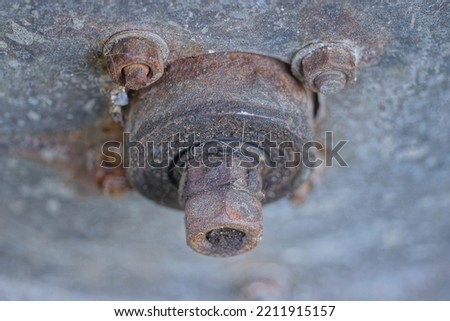 brown rusty iron bolts and nuts with an axle on a gray metal panel