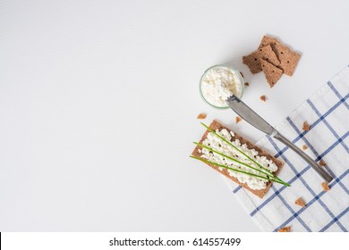 Brown Rye Crispy Bread (Swedish Crackers) With Spread Cottage Cheese, Decorated With Thin Green Onion, On Piece Of Cloth On White Background With Space For Text, Top View. Healthy Snack Concept