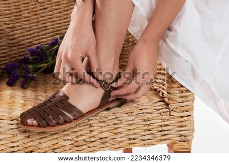 A brown sandal shoe's and it lace highlighted weared by a model in the chair made with bamboo  with a decorative flower in the background 