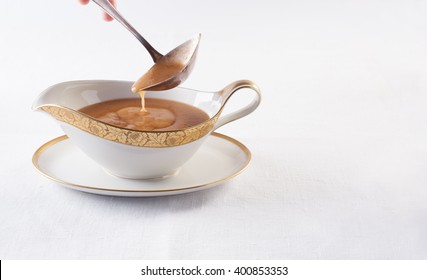 Brown Sauce Is Poured Into A Spoon In A White Gravy Boat On A White Tablecloth, Horizontal