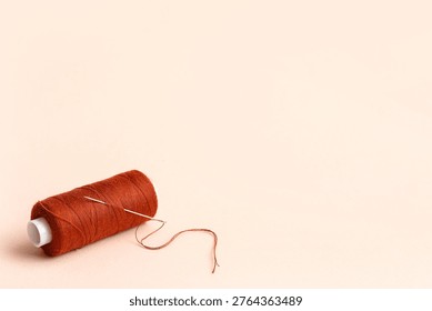 Brown sewing thread with needle on beige background