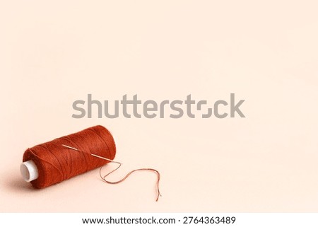 Brown sewing thread with needle on beige background