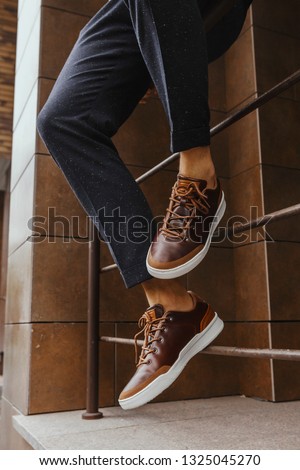 Brown sneakers or shoes with white sole and dark blue pants on men's lags close up. industrial background