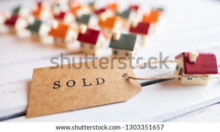 Brown SOLD stamped text label tag with miniature houses on wooden white board. Conceptual image. Selective focus.