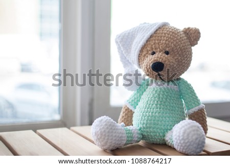 Brown stuffed animal teddy bear in lilac clothes and white hat on the wood.