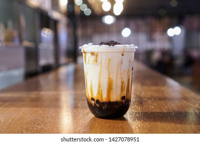Brown sugar bubble drink. A plastic cup of fresh milk and brown sugar boba/bubble toppings and topped with chocolate cookies on wooden table.