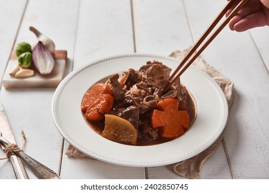 A brown tablecloth was spread on a white wooden table, and steamed pork ribs with flower-shaped carrots were placed on a ceramic plate and served with kimchi using wooden chopsticks. - Powered by Shutterstock