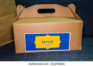 A Brown Takeout Cardboard Box With A 'Family Feast' Sticker Tag. 