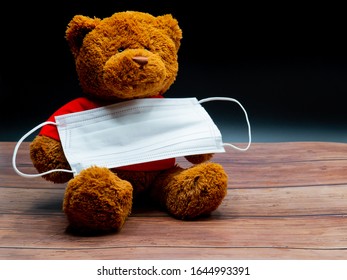 A Brown Teddy Bear Holding A Surgical Mask For Protection Of Infection On The Black Background. Coronavirus, Covid 19, Protection, Prevention, Quarantine, Medical, Child Safety Concept