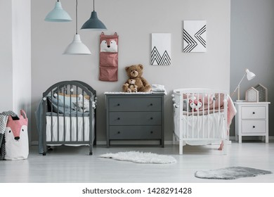 Brown Teddy Bear On Grey Wooden Commode Between Two Cribs In Fashionable Bedroom For Twins