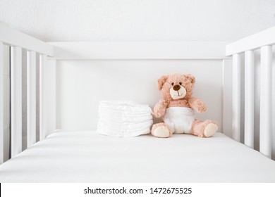 Brown teddy bear with white diaper sitting in baby bed.
