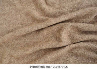 Brown textured background made of hand-knitted natural wool yarn. Warm cozy knitted clothes or handmade plaid, top view. Down shawl made of goat or sheep wool. Pleats, draperies