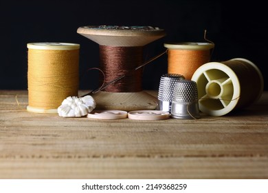BROWN THREAD WITH NEEDLE ON AN OLD WOODEN SPOOL WITH YELLOW HUED THREAD ON MODERN REELS