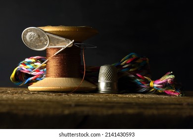 BROWN THREAD ON AN OLD WOODEN COTTON REEL THREADED THROUGH A NEEDLE THREADER WITH BRIGHT THREAD BRAID AND THIMBLE