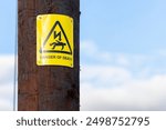 Brown timber telegraph pole with yellow danger of death warning sign