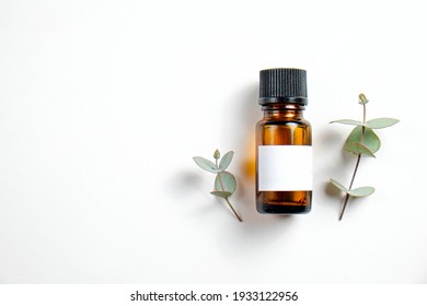 Brown transparent glass bottle with black cap and blank label with copy space for text or logo, white wood textured table background. Essential oils for aroma therapy. Close up, copy space, top view.
