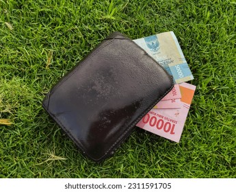 brown wallet filled with indonesian money on the grass, can be used for finance wallpaper - Shutterstock ID 2311591705