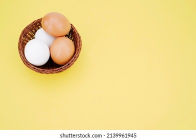 Brown And White Eggs In A Wicker Canister Top View On A Yellow Table Surface With Space For Text