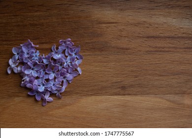 Brown wood background with heart of purple lilac flowers, empty template for text