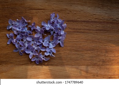 Brown wood background with heart of purple lilac flowers.