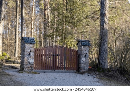 brown wooden cemetery gate with stone columns. Latvian forest graveyards.