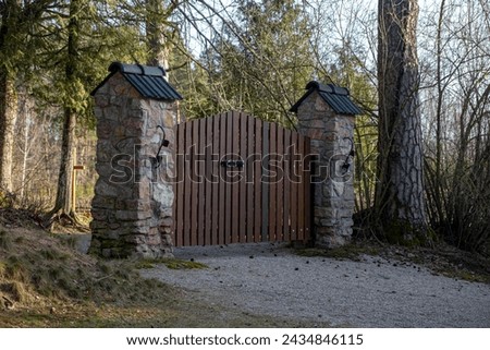 brown wooden cemetery gate with stone columns. Latvian forest graveyards.